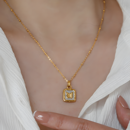 Gold necklace with a butterfly pendant worn by a person in a white outfit.