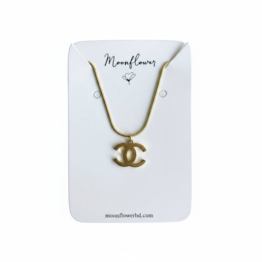 Gold necklace with a CC pendant on a 'Moonflower' branded card against a wooden background