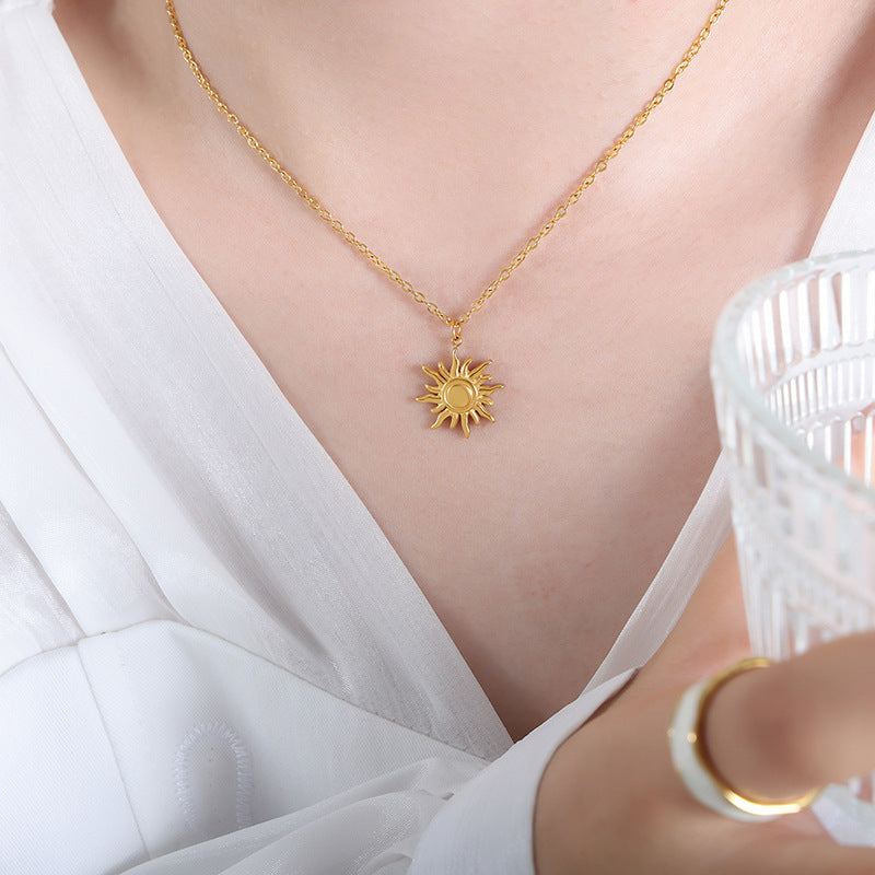 Gold necklace with a sun pendant worn by a person in a white outfit.