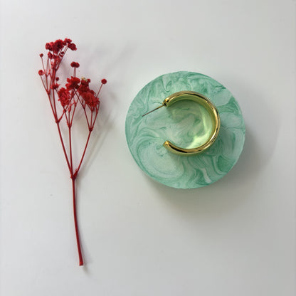 Gold hoop earring on a green marbled stand with red flowers on a white background