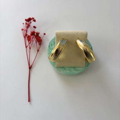 Gold earrings on a green stand with a red flower on a white background