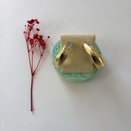 Gold earrings on a green stand with a red flower on a white background