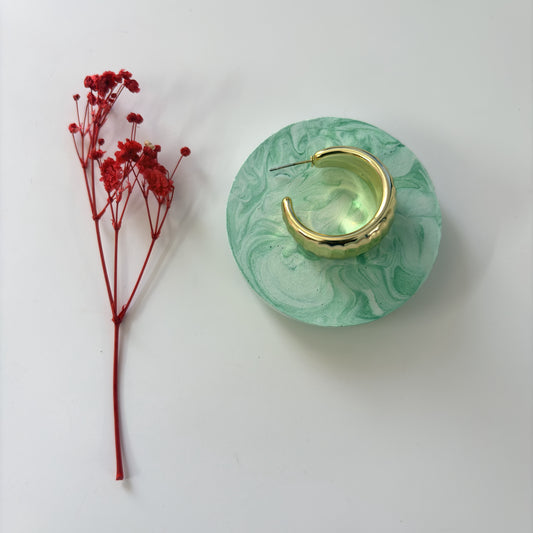 Gold hoop earring on a green marbled stand with red flowers on a white background