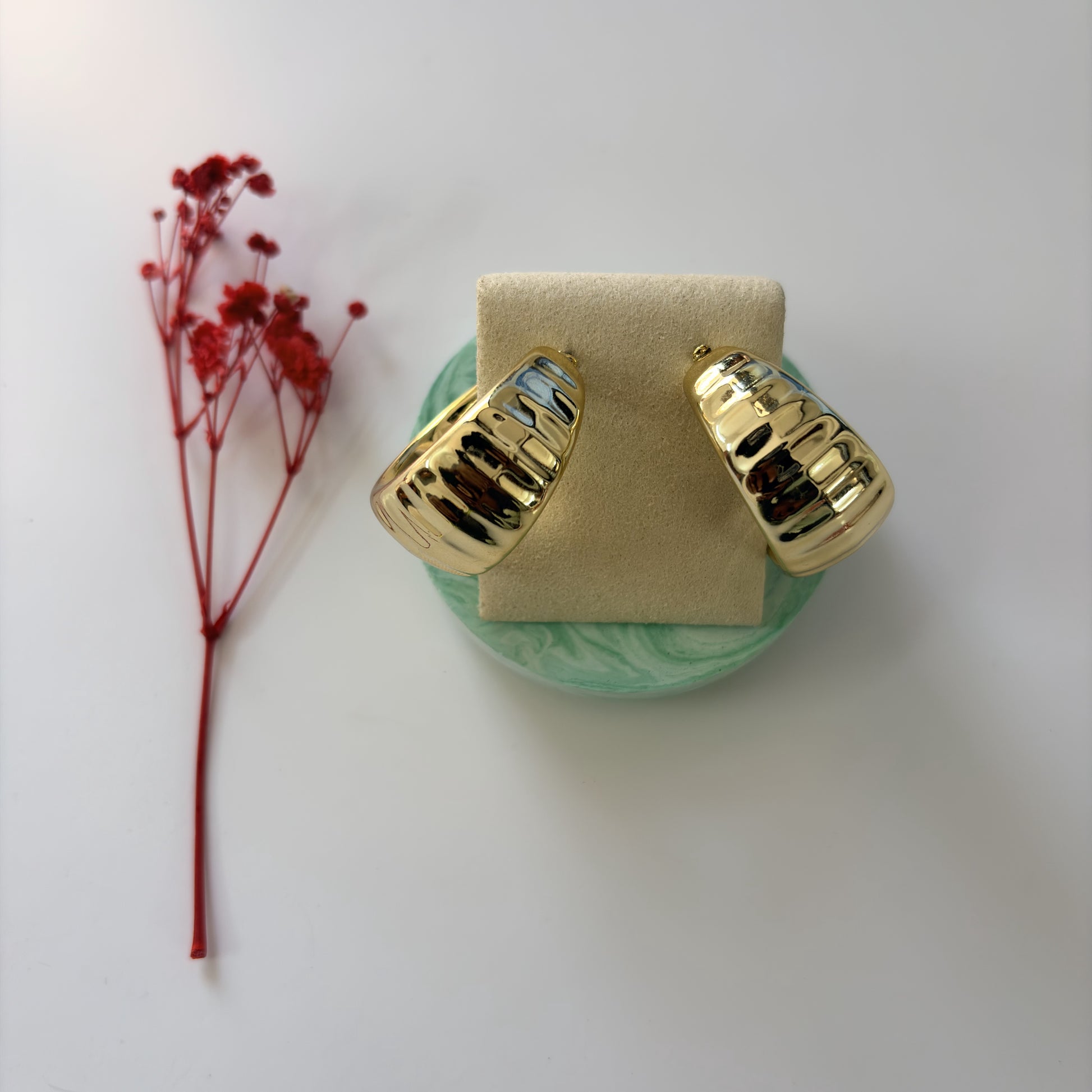 Gold earrings on a green stand with red flowers on a white background